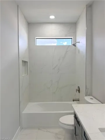 Bathroom with vanity, shower / bath combination, and light marble finish floors