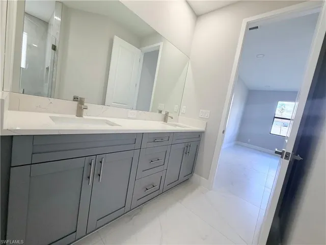 Full bathroom with double vanity, light marble finish flooring, and a shower stall