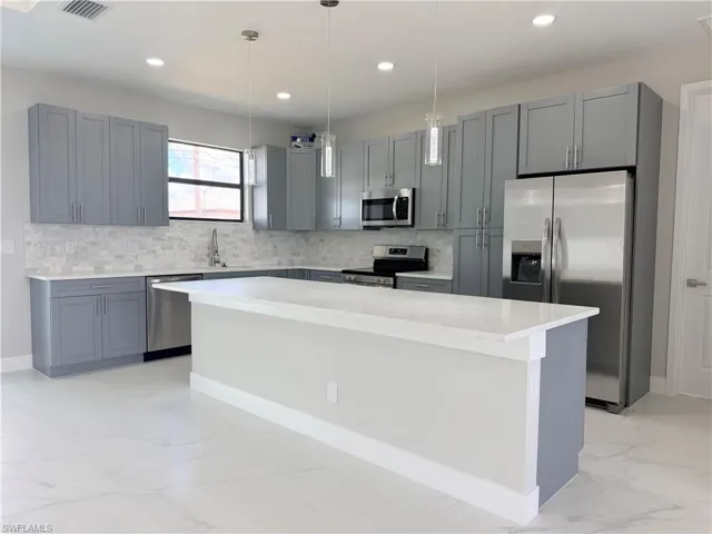 Kitchen with stainless steel appliances, gray cabinetry, decorative backsplash, and a kitchen island