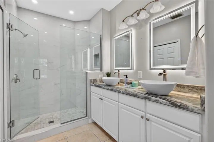 Bathroom featuring double vanity, a marble finish shower, light tile patterned flooring, and recessed lighting
