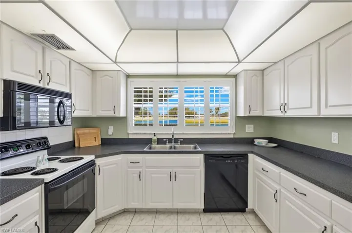 Kitchen featuring white cabinets, sink, black appliances, and light tile floors