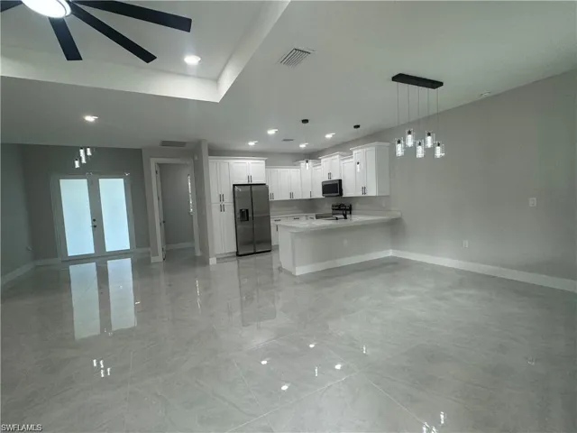 Kitchen featuring hanging light fixtures, a tray ceiling, white cabinetry, appliances with stainless steel finishes, and light tile floors