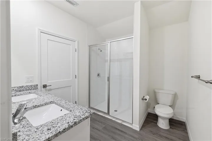Bathroom featuring double vanity, a stall shower, and dark wood finished floors