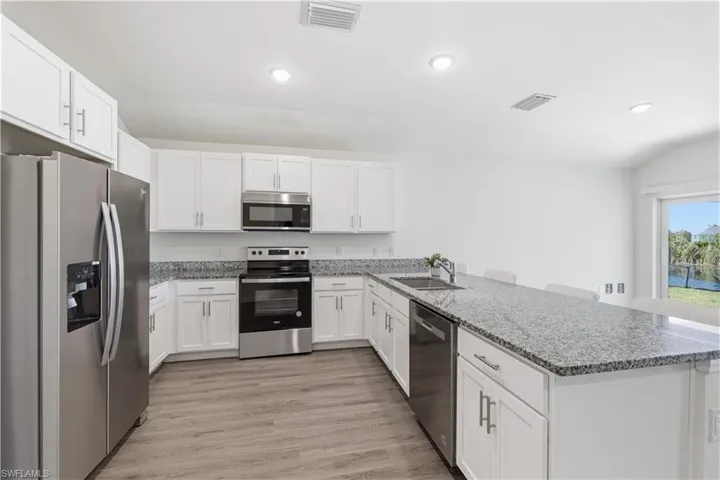 Kitchen featuring stainless steel appliances, a peninsula, white cabinets, a kitchen bar, and recessed lighting