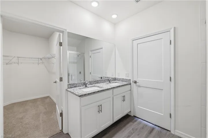 Full bathroom with double vanity, a walk in closet, light wood-style flooring, and a shower stall