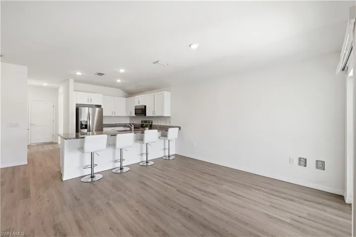 Kitchen featuring a peninsula, a kitchen breakfast bar, stainless steel appliances, white cabinetry, and light wood-type flooring
