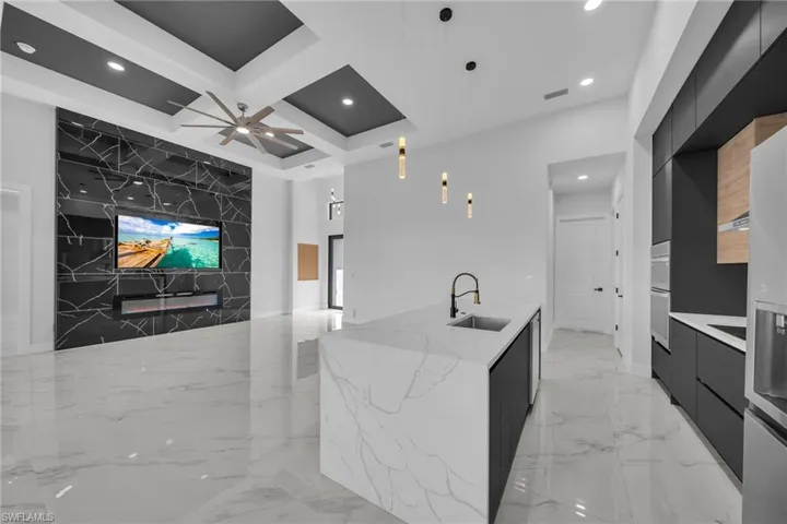 Kitchen with sink, hanging light fixtures, ceiling fan, a large island, and light stone counters