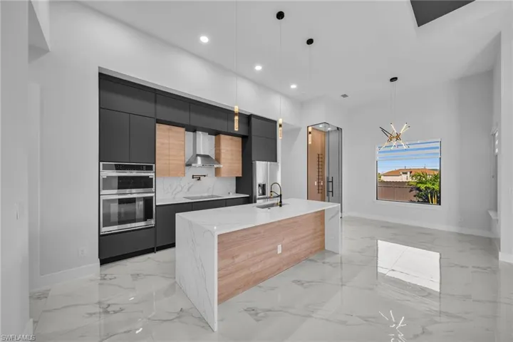 Kitchen with wall chimney range hood, backsplash, a spacious island, decorative light fixtures, and appliances with stainless steel finishes