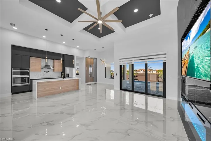 Kitchen featuring a center island with sink, hanging light fixtures, wall chimney exhaust hood, ceiling fan, and tasteful backsplash