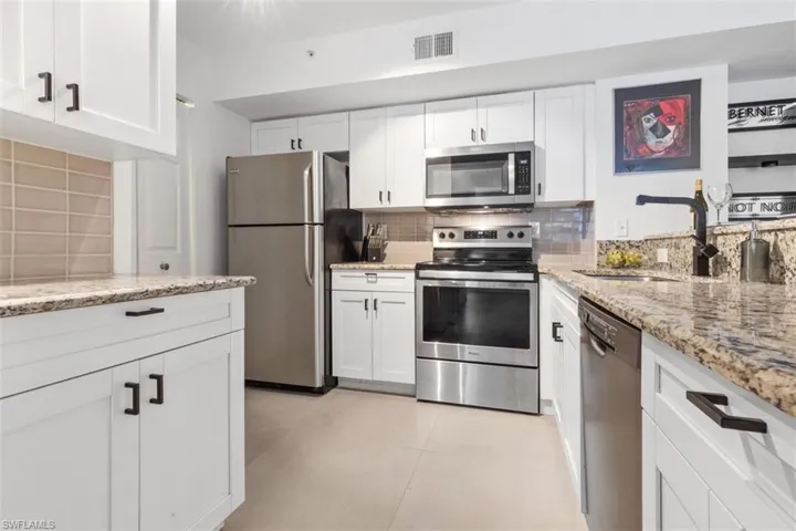 Kitchen with stainless steel appliances, white cabinets, light stone counters, sink, and tasteful backsplash