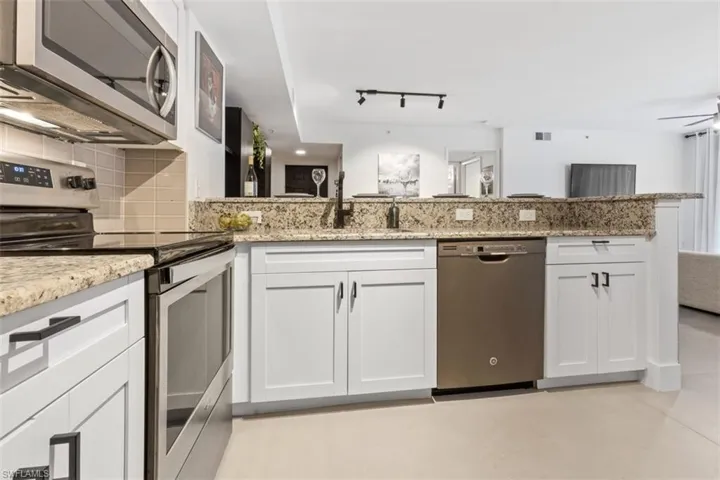 Kitchen featuring kitchen peninsula, stainless steel appliances, light stone counters, rail lighting, and white cabinetry