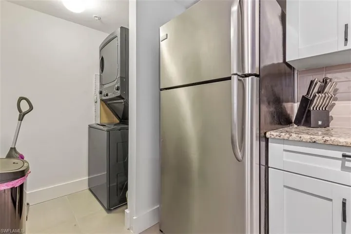Washroom with light tile floors and stacked washer / drying machine