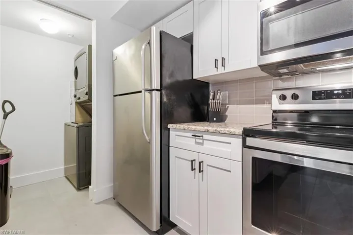 Kitchen with white cabinetry, stainless steel appliances, stacked washing maching and dryer, backsplash, and light tile floors