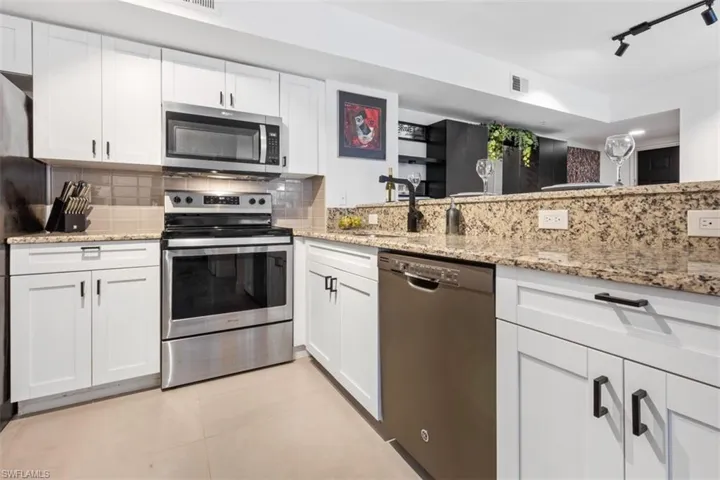 Kitchen featuring stainless steel appliances, backsplash, white cabinetry, and light tile floors