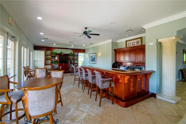 Kitchen featuring ceiling fan, crown molding, decorative columns, light tile flooring, and a kitchen bar