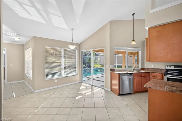 Kitchen featuring decorative light fixtures, light tile patterned flooring, dark stone countertops, appliances with stainless steel finishes, and high vaulted ceiling