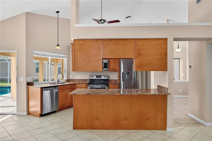Kitchen featuring decorative light fixtures, high vaulted ceiling, a ceiling fan, dark stone countertops, and appliances with stainless steel finishes