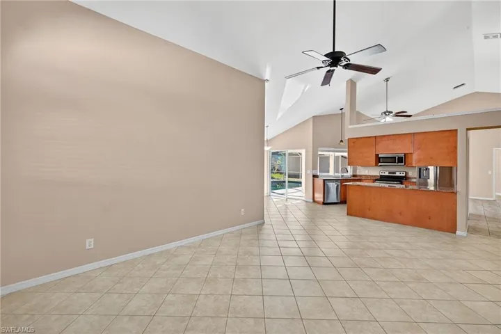 Kitchen featuring open floor plan, brown cabinetry, light tile patterned floors, stainless steel appliances, and a ceiling fan