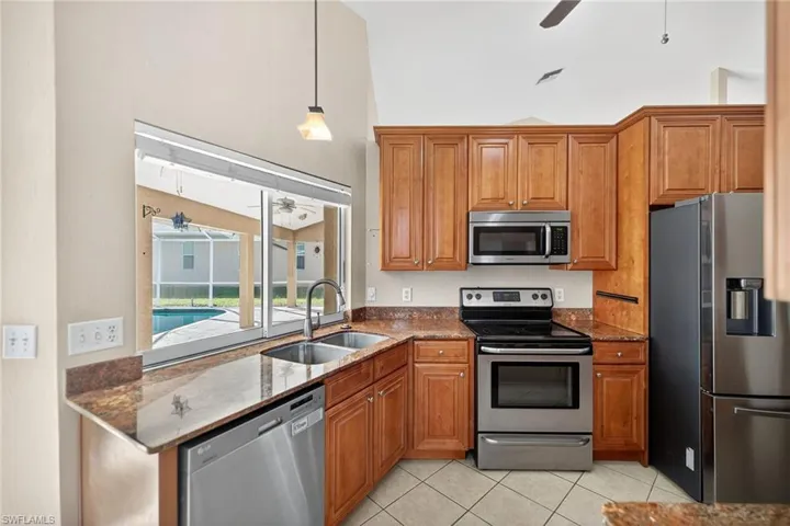 Kitchen featuring a ceiling fan, brown cabinetry, stainless steel appliances, and dark stone counters