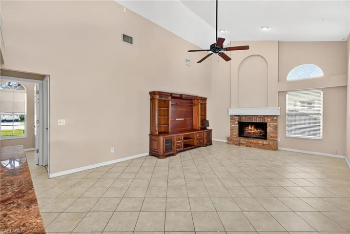 Unfurnished living room featuring healthy amount of natural light, high vaulted ceiling, a fireplace, light tile patterned flooring, and a ceiling fan