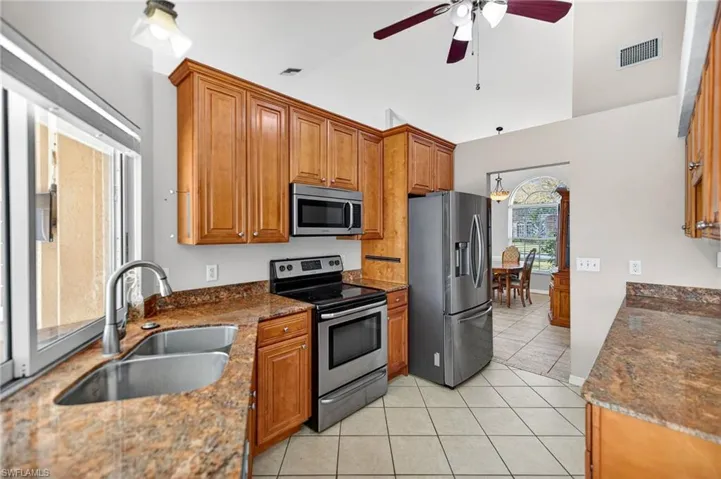 Kitchen with appliances with stainless steel finishes, dark stone countertops, brown cabinets, light tile patterned floors, and lofted ceiling