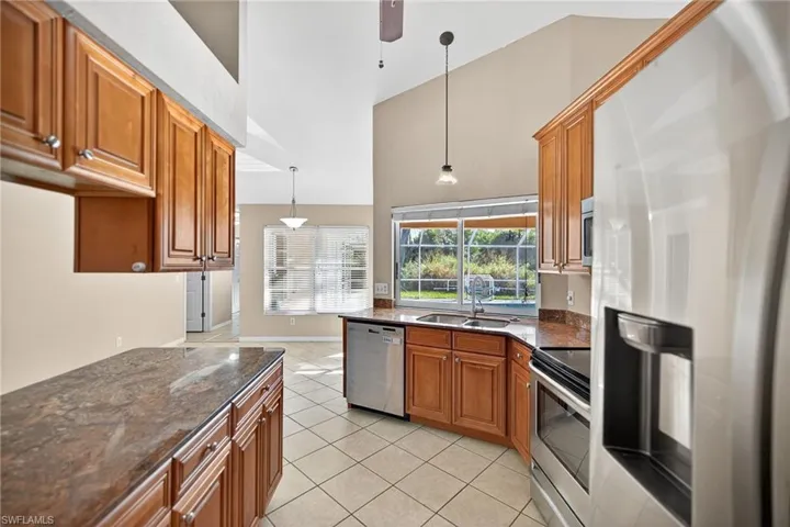 Kitchen with appliances with stainless steel finishes, dark stone countertops, brown cabinets, decorative light fixtures, and light tile patterned floors
