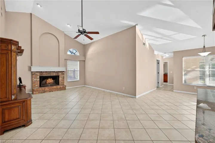Unfurnished living room featuring high vaulted ceiling, light tile patterned flooring, a fireplace, and a ceiling fan