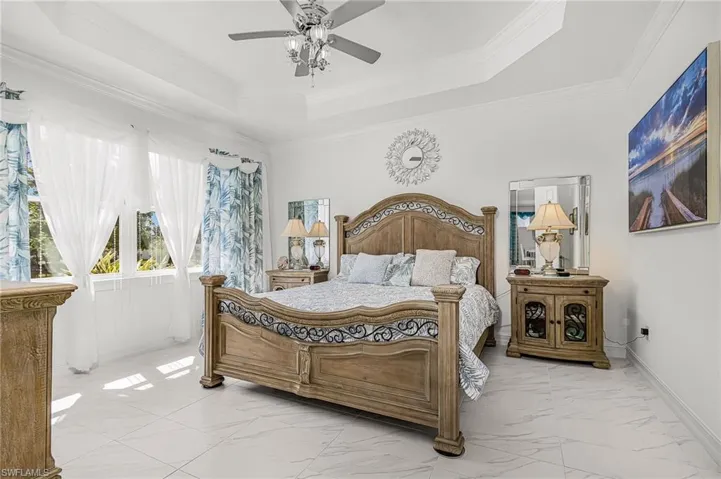 Tray ceiling with a ceiling fan, white tile flooring, and large windows with transom elements