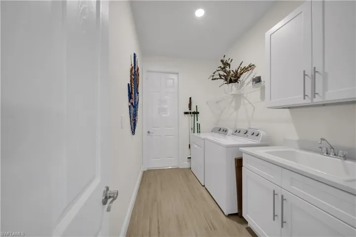 Laundry room with washing machine and clothes dryer, light wood-style floors, cabinet space, baseboards, and recessed lighting