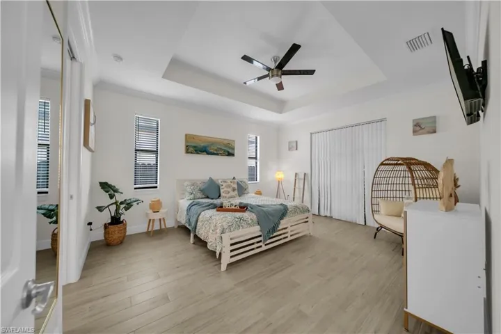 Bedroom with a raised ceiling, light wood-style floors, a ceiling fan, baseboards, and ornamental molding