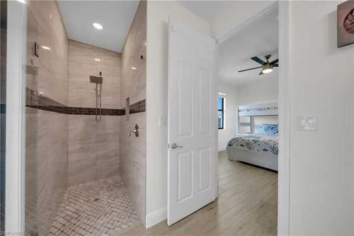 Ensuite bathroom with tiled shower, wood finished floors, ceiling fan, baseboards, and recessed lighting