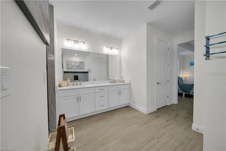 Bathroom with connected bathroom, double vanity, wood finished floors, and baseboards