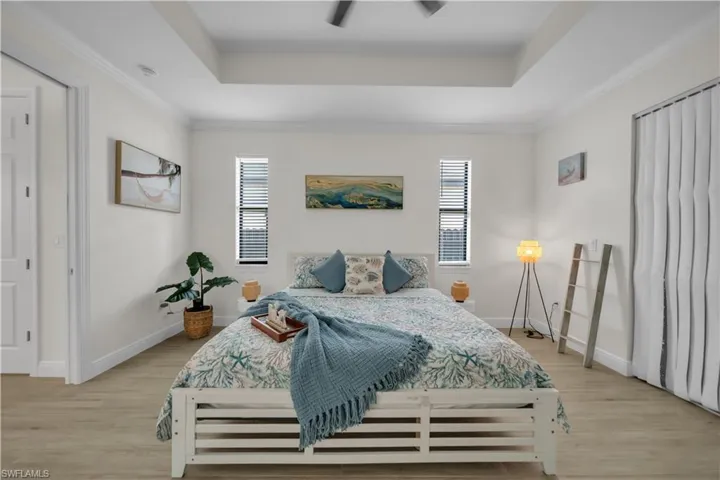Bedroom featuring a tray ceiling, light wood-style floors, baseboards, and crown molding