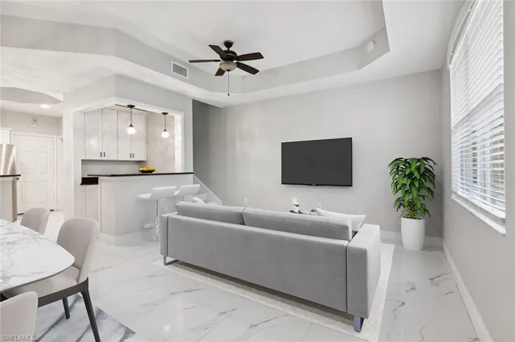 Living room featuring a raised ceiling, ceiling fan, and light tile floors