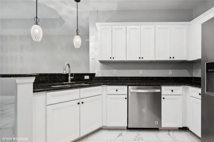 Kitchen featuring dishwasher, decorative light fixtures, dark stone countertops, light tile floors, and white cabinets