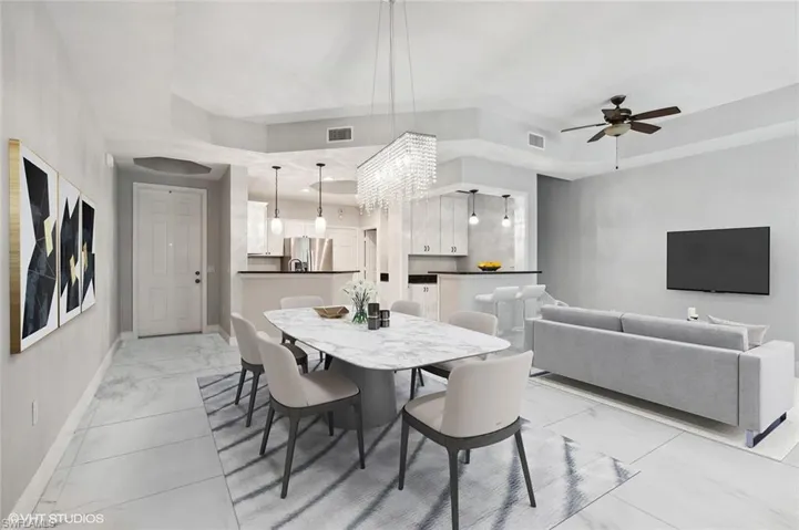Dining area featuring a tray ceiling, light tile floors, and ceiling fan with notable chandelier