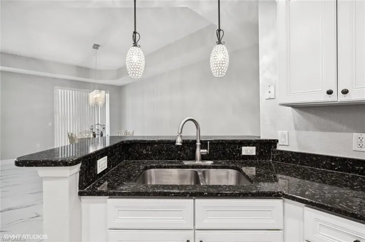 Kitchen featuring white cabinets, decorative light fixtures, and dark stone countertops