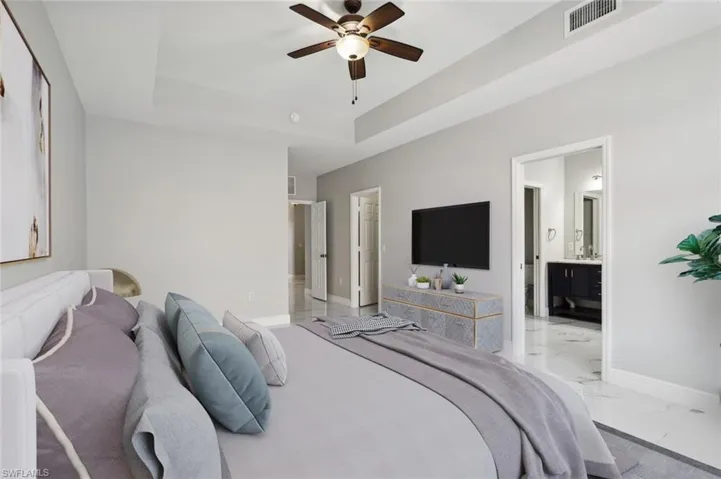 Bedroom with ensuite bathroom, ceiling fan, light tile floors, and a raised ceiling