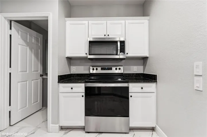 Kitchen featuring dark stone countertops, stainless steel appliances, white cabinets, and light tile floors
