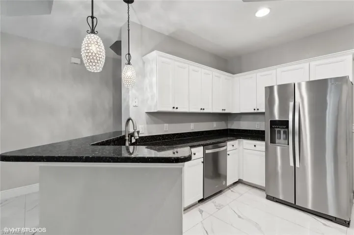 Kitchen featuring kitchen peninsula, stainless steel appliances, decorative light fixtures, light tile floors, and white cabinets