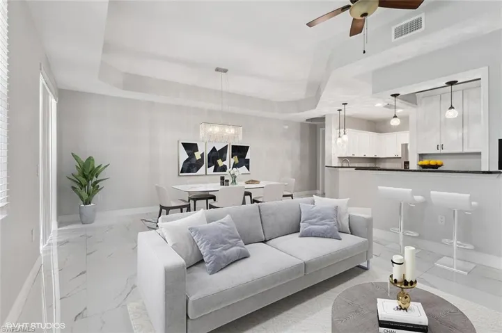 Tiled living room with ceiling fan with notable chandelier and a tray ceiling