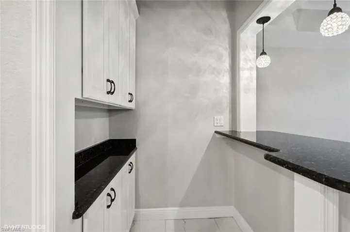 Kitchen with hanging light fixtures, white cabinets, dark stone countertops, and light tile floors