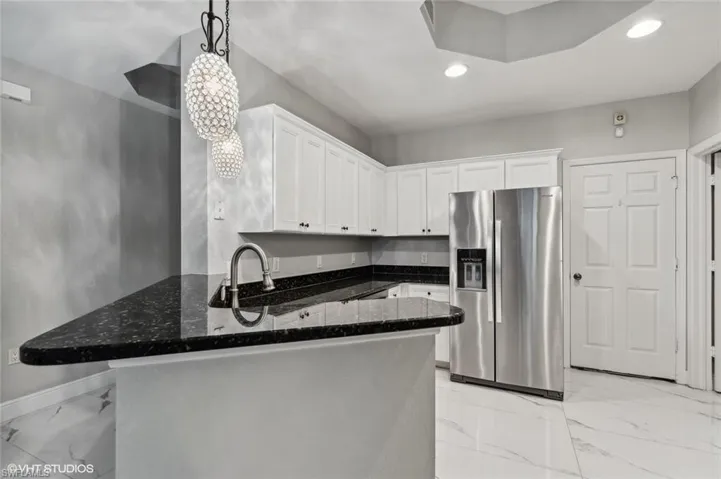 Kitchen featuring decorative light fixtures, stainless steel fridge with ice dispenser, white cabinets, and kitchen peninsula
