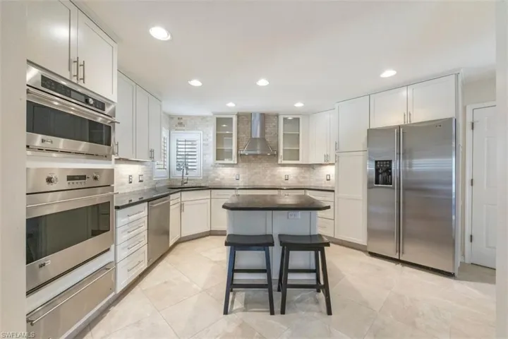 Modern Updated Kitchen with appliances with stainless steel finishes, white cabinetry, a center island, a warming drawer, and wall chimney range hood