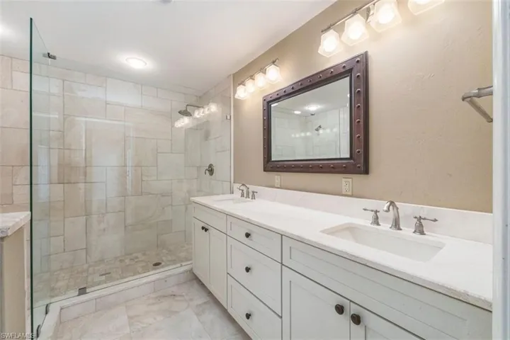 Bathroom with double vanity, a stall shower, and light marble finish flooring