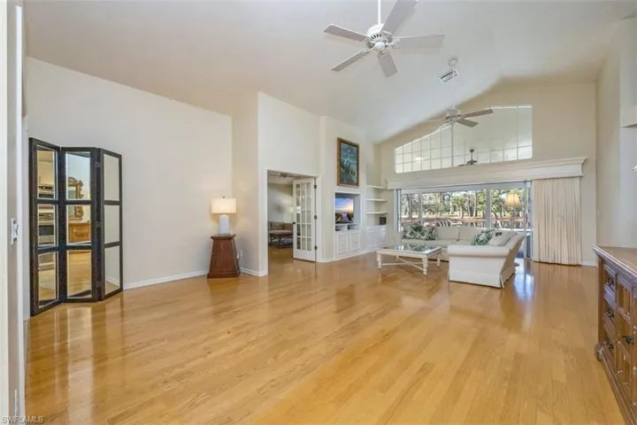 Living room featuring light wood-type flooring, built in features, high vaulted ceiling, and ceiling fan