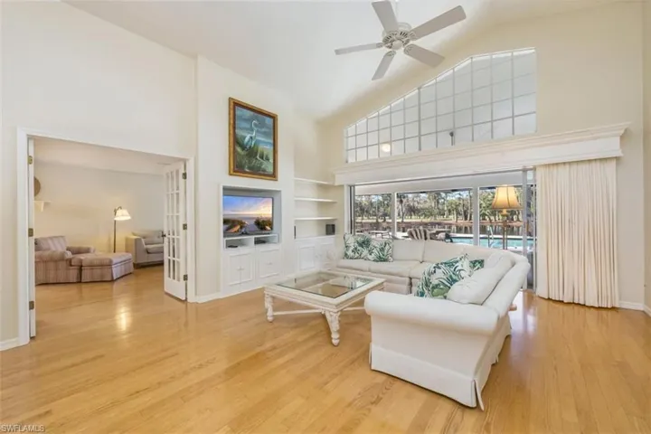 Living room featuring high vaulted ceiling, built in shelves, light wood finished floors, and ceiling fan