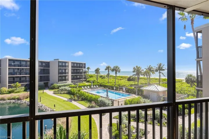 Screened-in balcony featuring a black metal railing, overlooking a swimming pool, manicured grounds, and the ocean shoreline