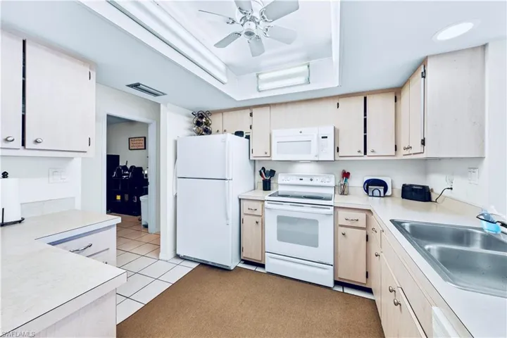 Kitchen featuring light carpet, sink, ceiling fan, and white appliances