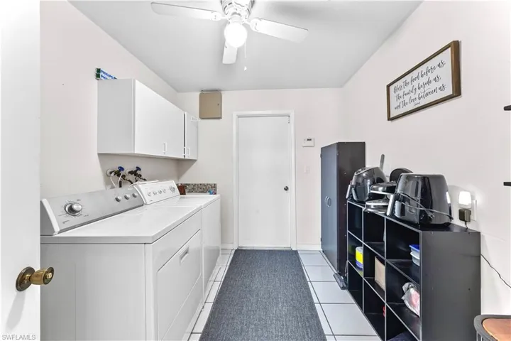 Washroom featuring washing machine and dryer, ceiling fan, light tile patterned floors, and cabinets